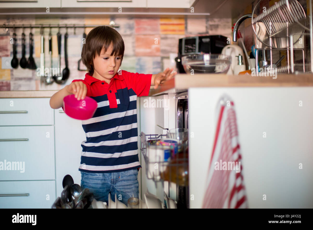 Preschool child, boy, helping mom, putting dirty dishes in dishwasher at home, modern kitchen Stock Photo