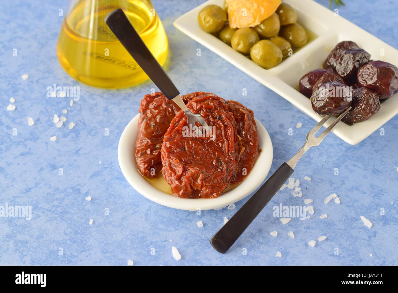 A set of dishes of greek cuisine: olives, sun dried tomatoes, lemon, glass jar with olive oil. Traditional Greek food. Mediterranean lifestyle Stock Photo