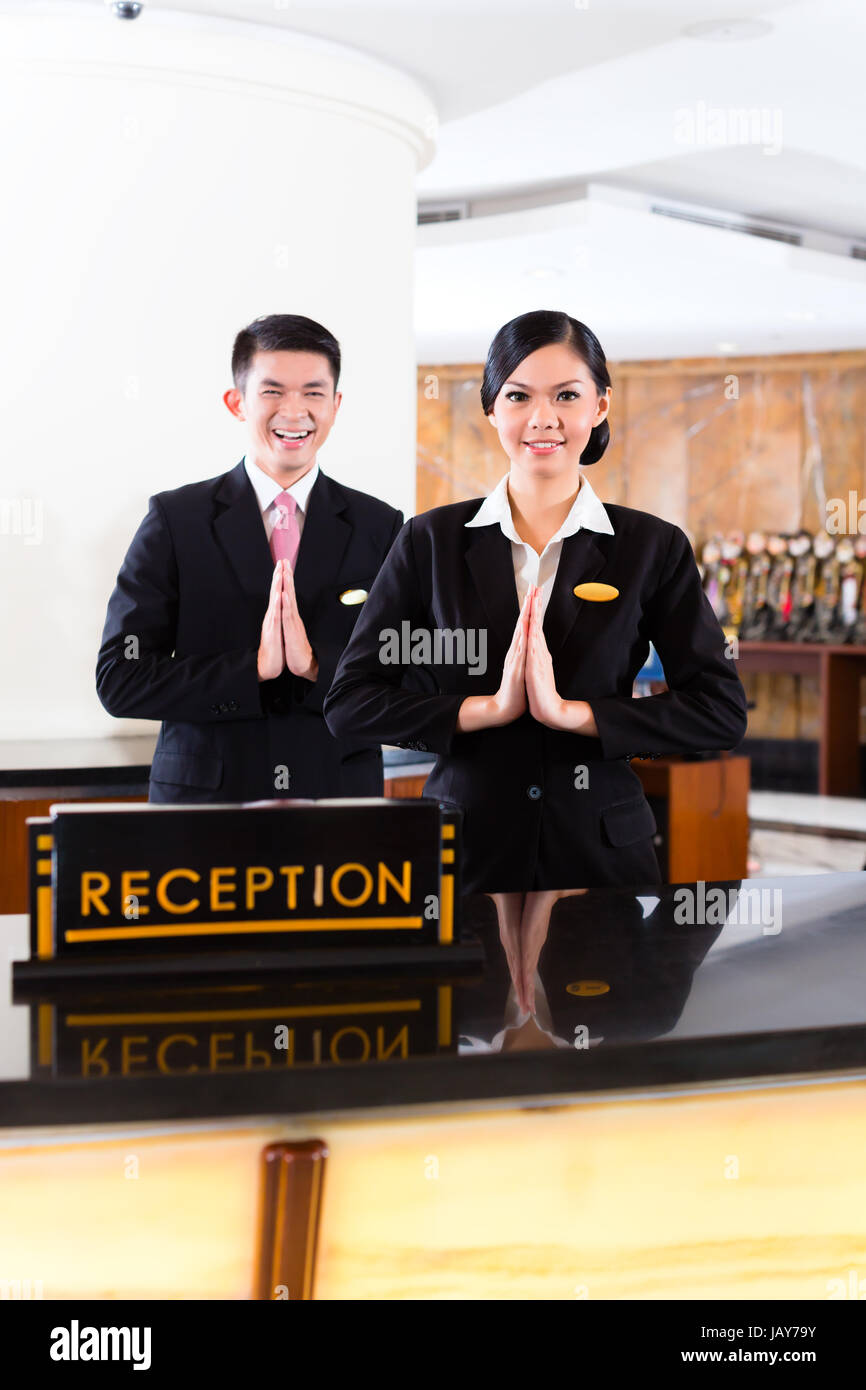 Chinese Asian reception team at luxury hotel front desk welcoming guests with typical gesture, a sign of good service and hospitality Stock Photo