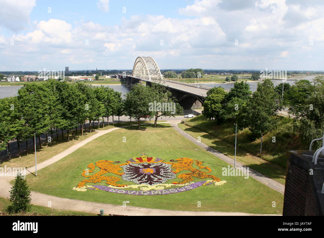 View over Waal river with Waalbrug arch bridge (1936), Nijmegen, Gelderland, Netherlands. Seen from Valkhof / Belvédère. City Coat of Arms in flowers. Stock Photo