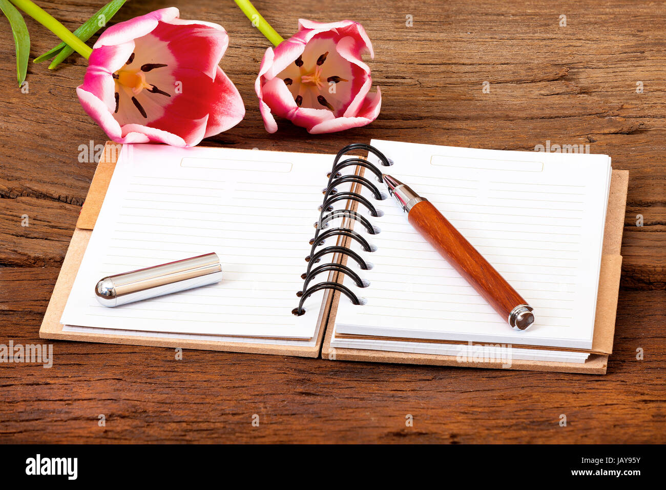 Notizbuch aufgeschlagen,ein Stift und zwei Tulpen liegen auf hölzernen Untergrund Stock Photo