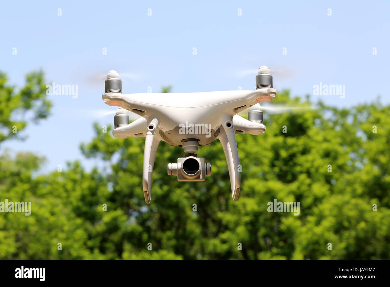 White remote controlled drone flying with clear blue sky with tree