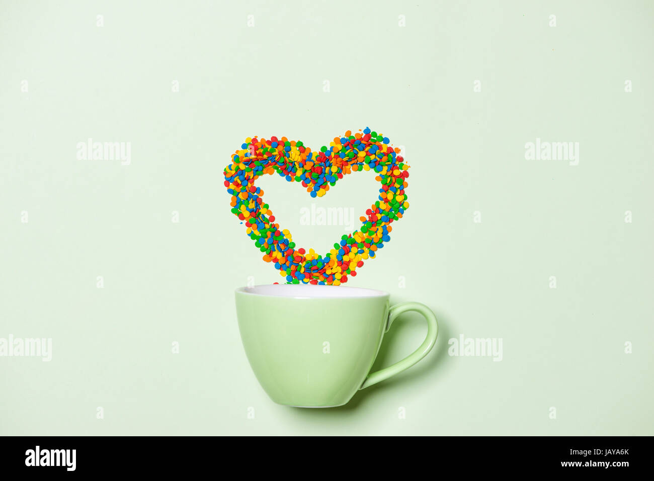 Cup of Cappuccino with heart shape symbol and candy on pastel green background Stock Photo