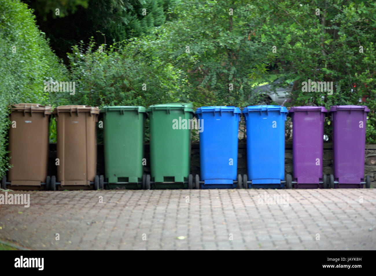 line of eight coloured refuse bins neat tidy clean in drive Stock Photo
