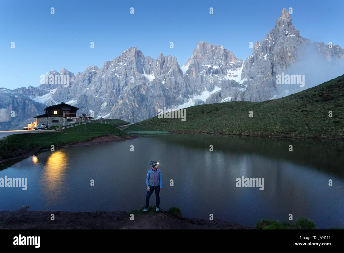 Woman standing at the lake at Rifugio Segantini with a head torch, Dolommites, Italy. Stock Photo