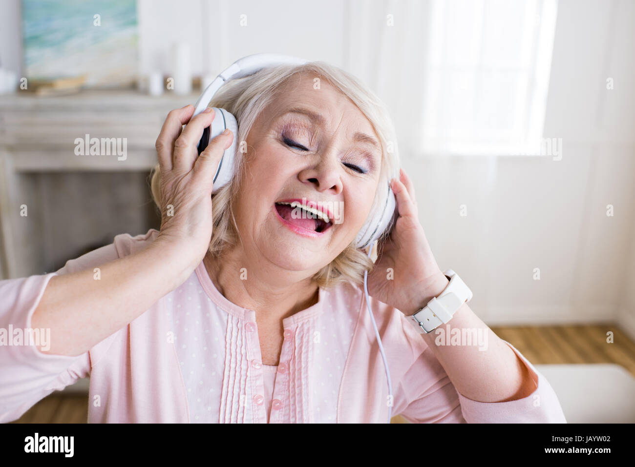 Happy senior woman with closed eyes wearing headphones and singing Stock Photo