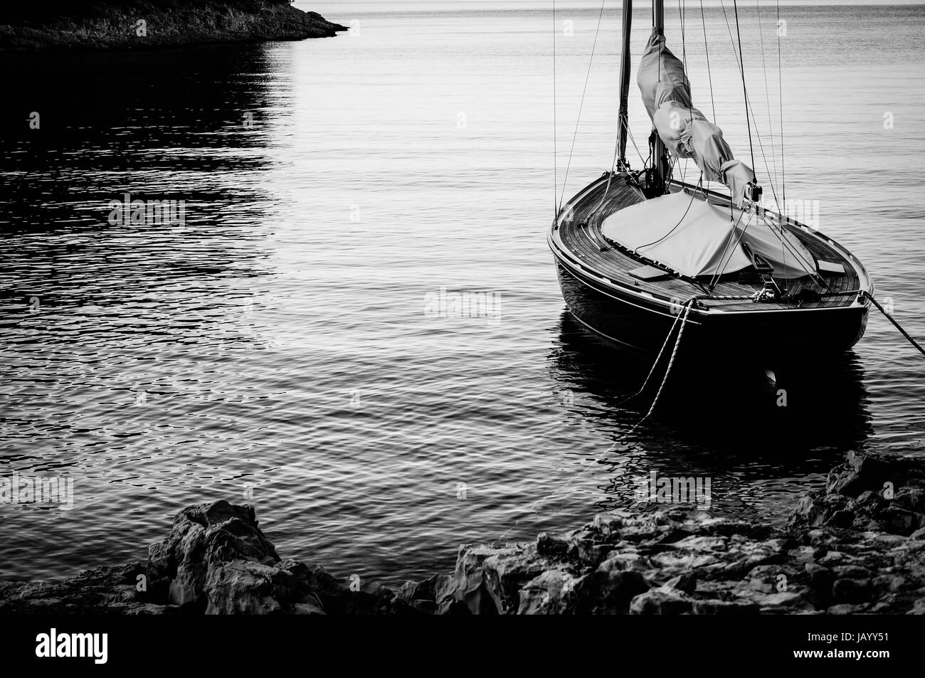 sailing boat anchoring and moored at land in calm water. yying in a calm bay in Croatia. Adriatic Sea. picture taken at sunset in black and white Stock Photo