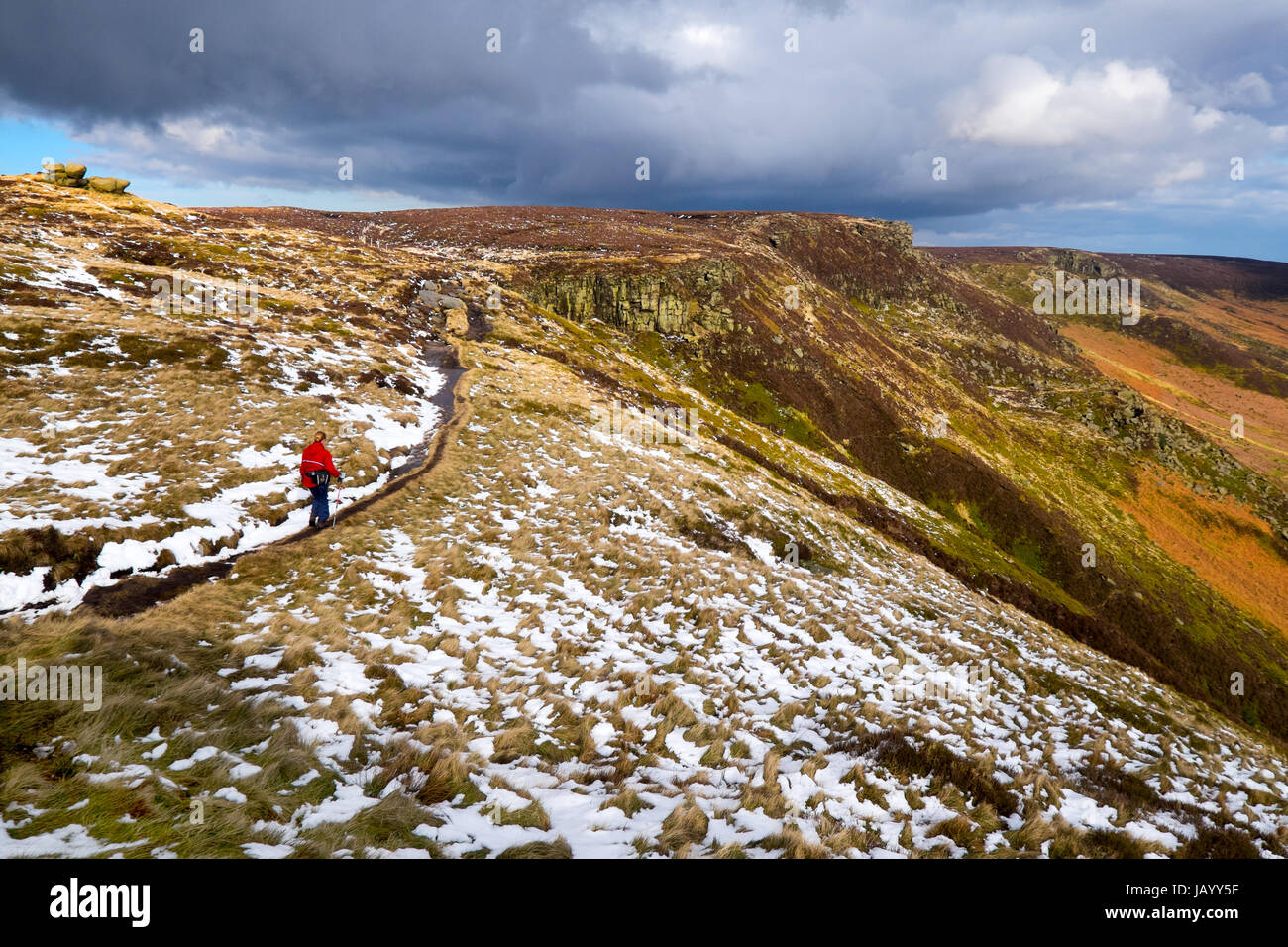 A female walker on the path along the southern edge of Kinder Scout in the Peak District National Park., with light snow on the ground Stock Photo