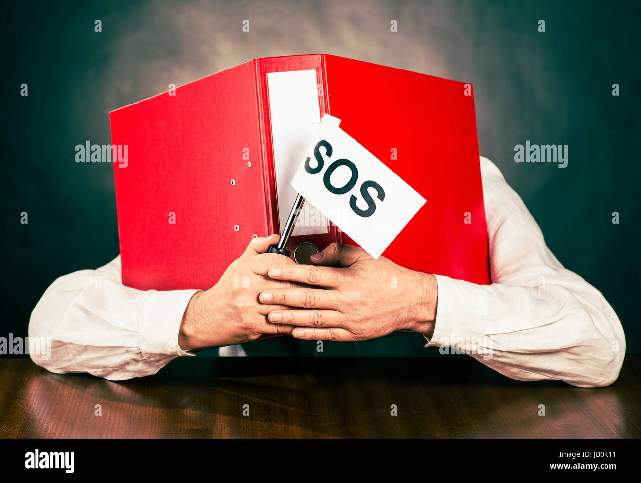 An employee hides his face behind a red file folder, holding an SOS flag in his hand. Stock Photo