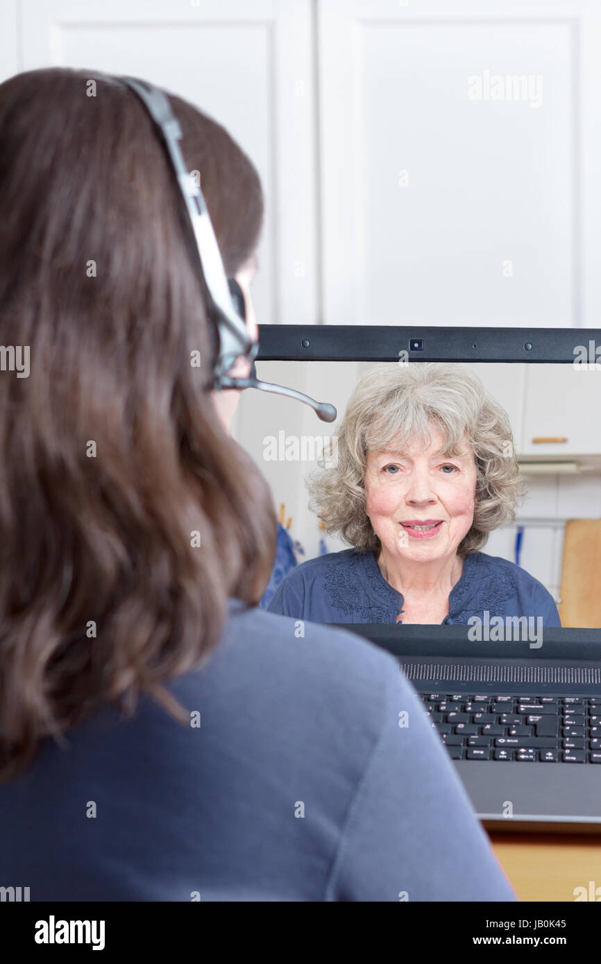 Woman with headset at her desk in front of her laptop making a video call with her grandmother, copy or text space Stock Photo