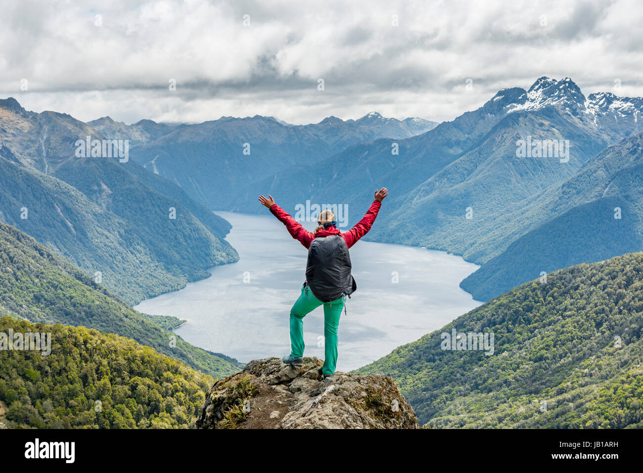 Female hiker is looking at the South Fiord of Lake Te Anau, stretching arms in the air, at back the Southern Alps Stock Photo