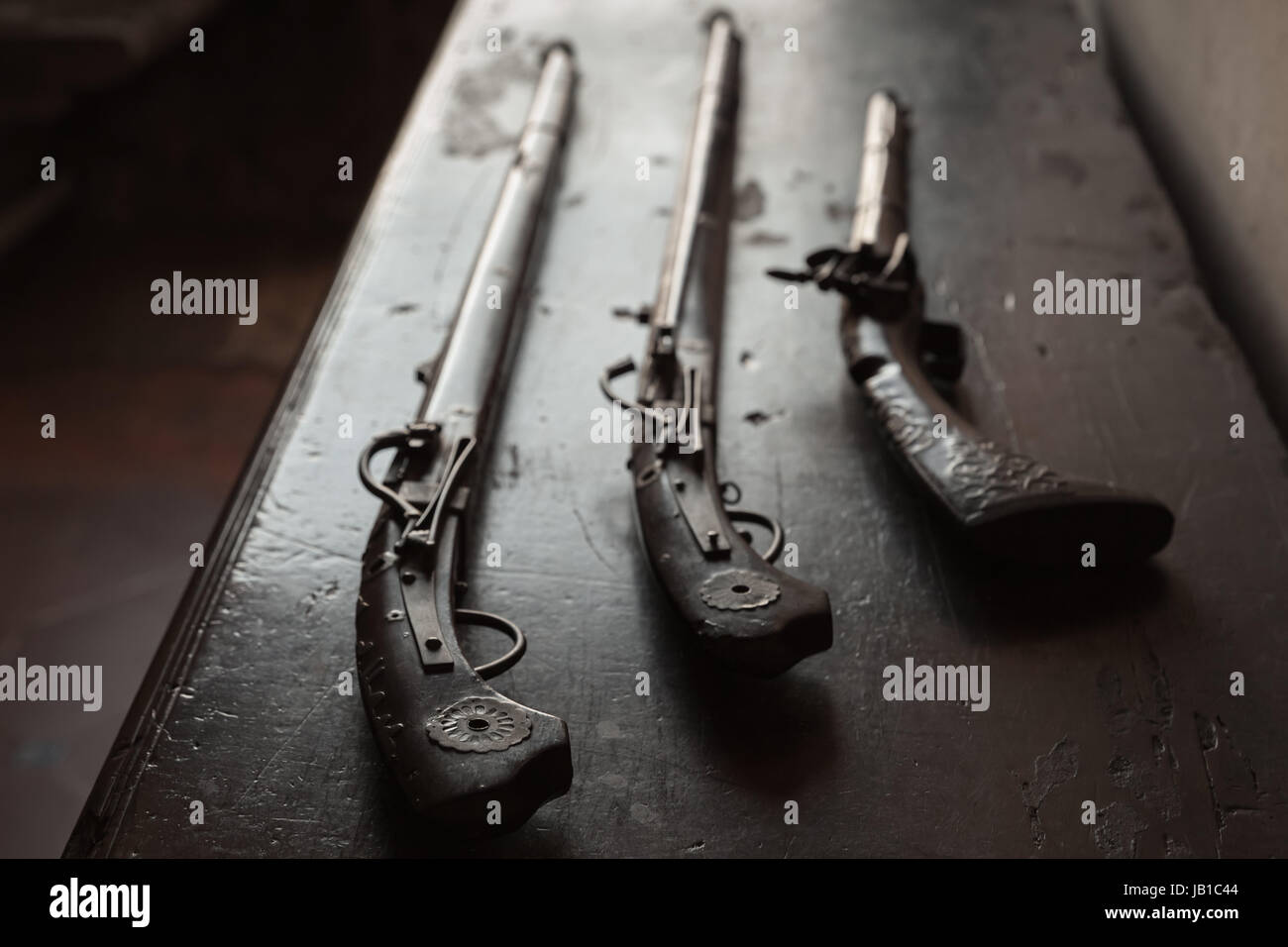 Three ancient guns lay on dark wooden table, closeup photo with selective focus Stock Photo