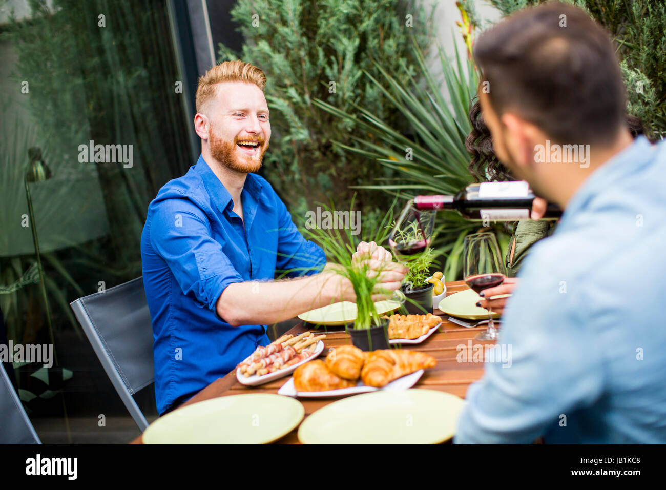View at two young men are sitting at the table and to drink red wine ...