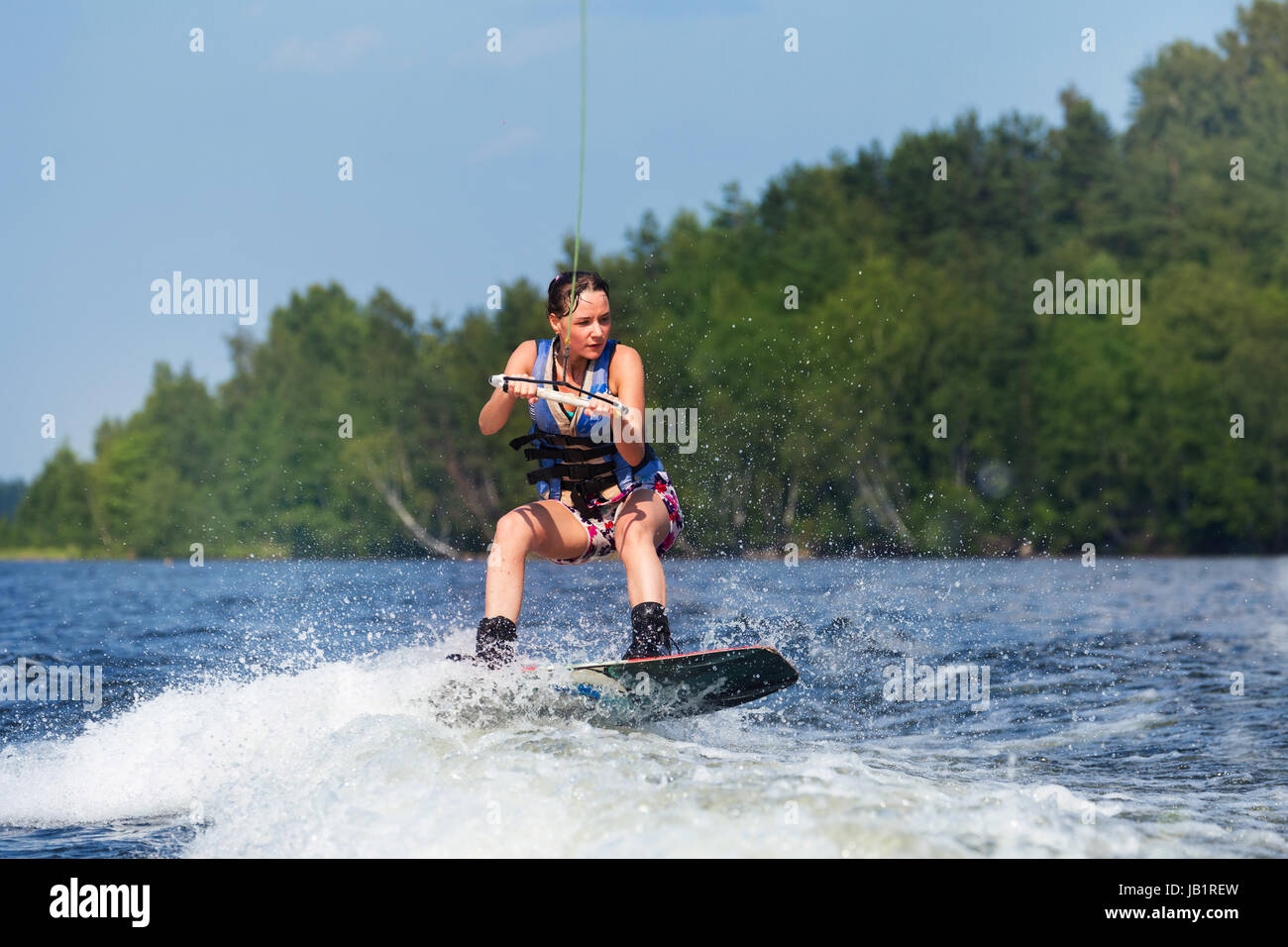 Young pretty slim brunette woman riding wakeboard on wave of motorboat in a summer lake Stock Photo