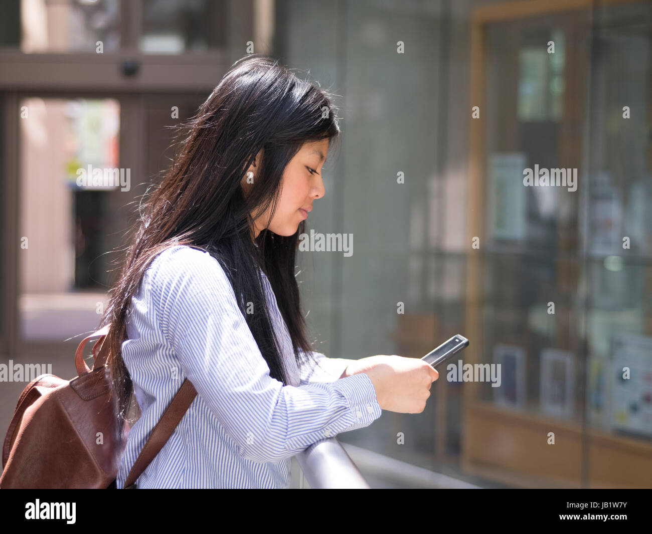 Smiling young Asian female student using her iphone at university campus Stock Photo