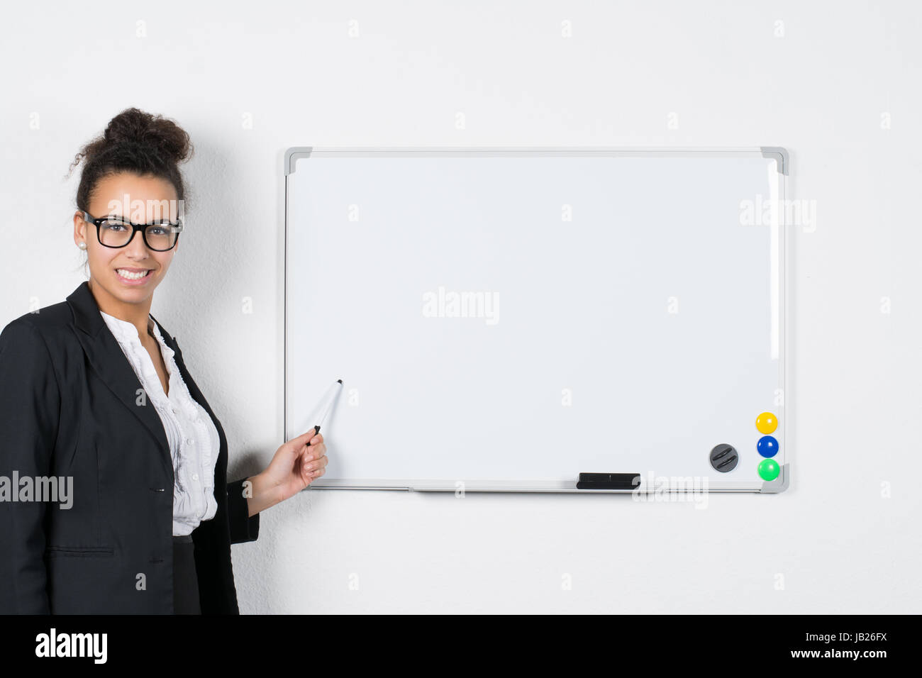 Junge Geschäftsfrau zeigt mit einem Stift auf eine weiße Magnet-Tafel Stock Photo