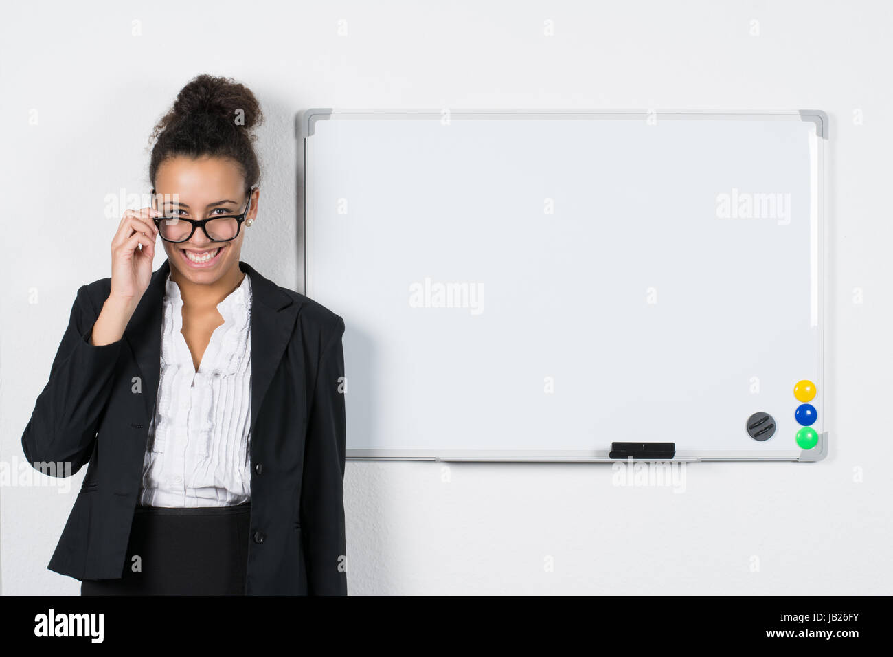 Junge Angestellte steht neben einer weiße Magnet-Tafel während sie ihre Brille hält Stock Photo