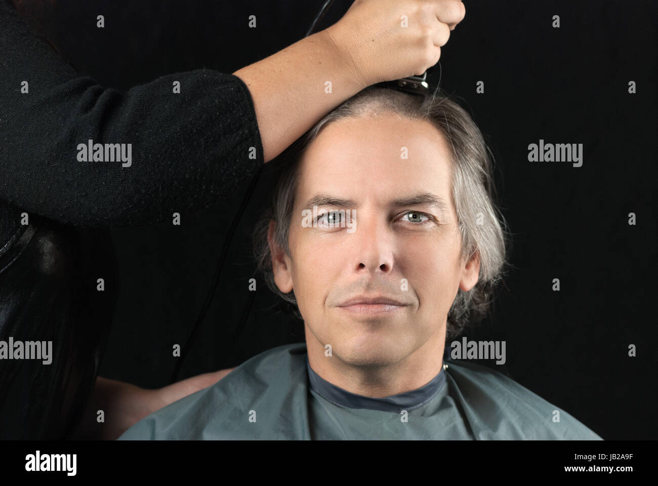 Close-up of a serious man looking to camera while his long hair is shaved off for a cancer fundraiser. Stock Photo