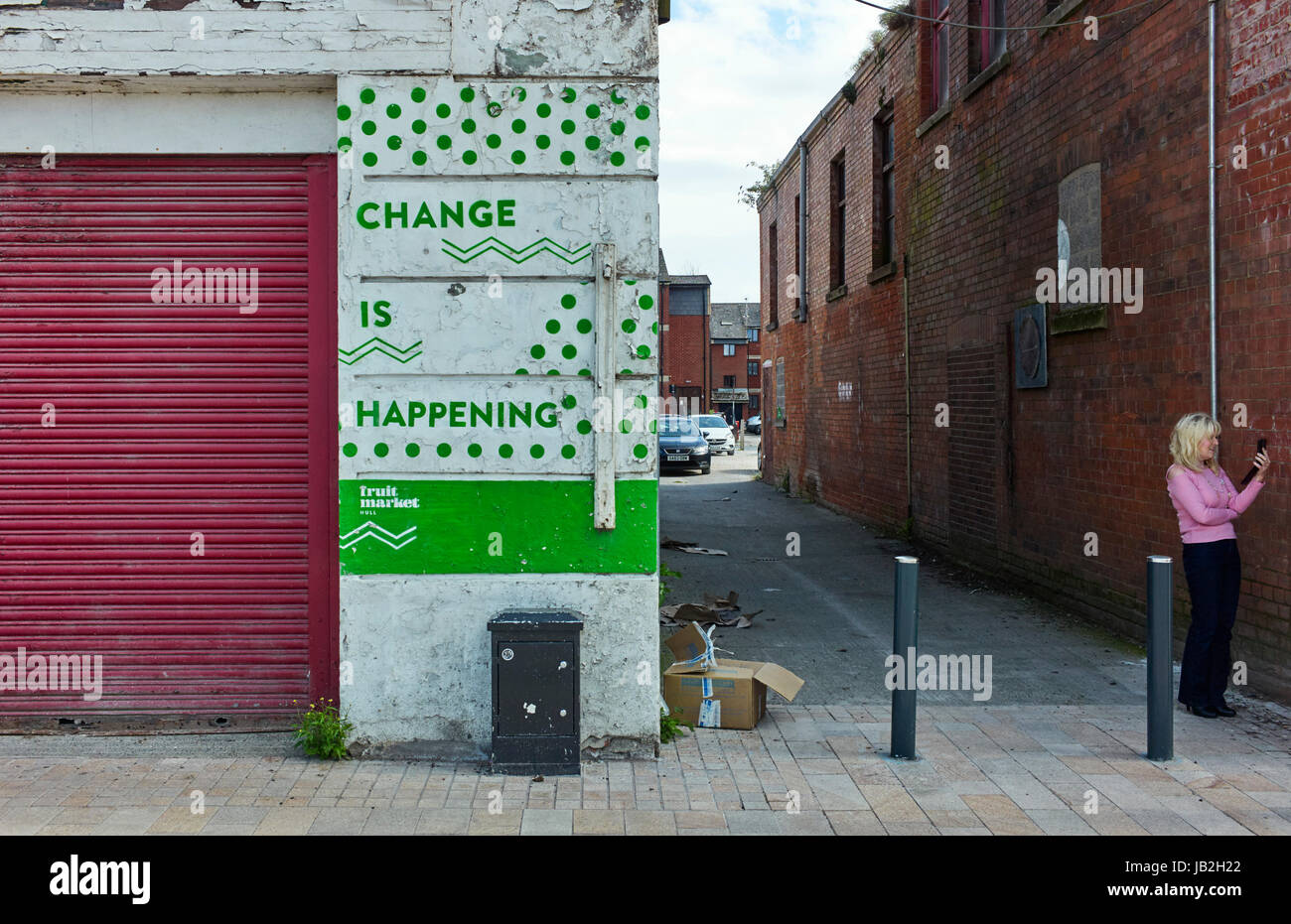 Woman looking at mobile phone next to change is happening sign in the fruit market area of Hull Stock Photo