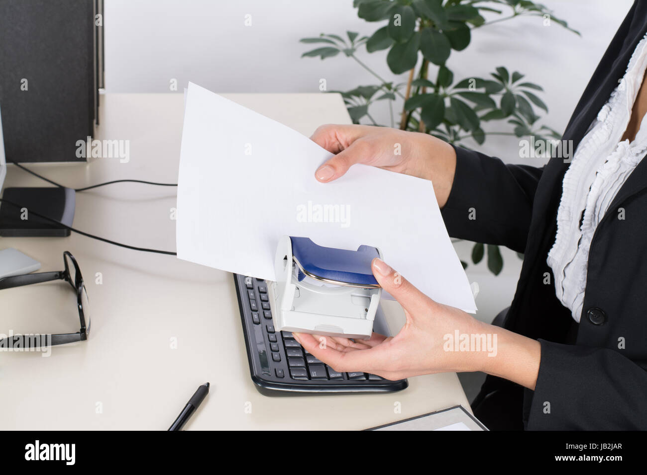 Junge Frau sitzt am Schreibtisch im Büro und locht Dokumente Stock Photo