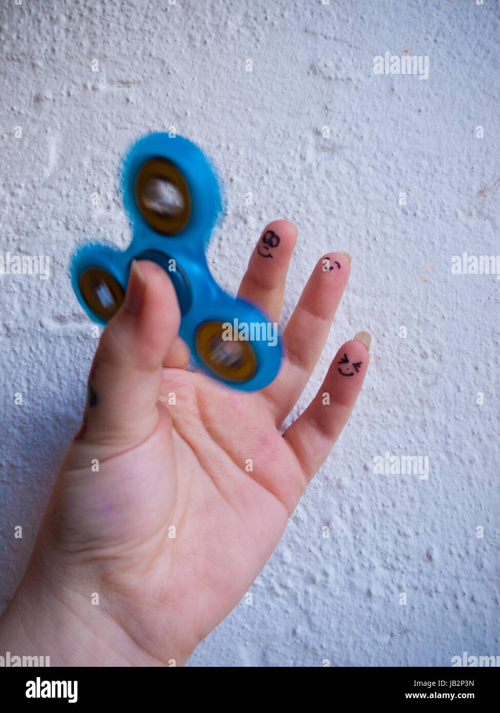 A moving fidget spinner in a hand with different smiling faces on the last three fingers Stock Photo