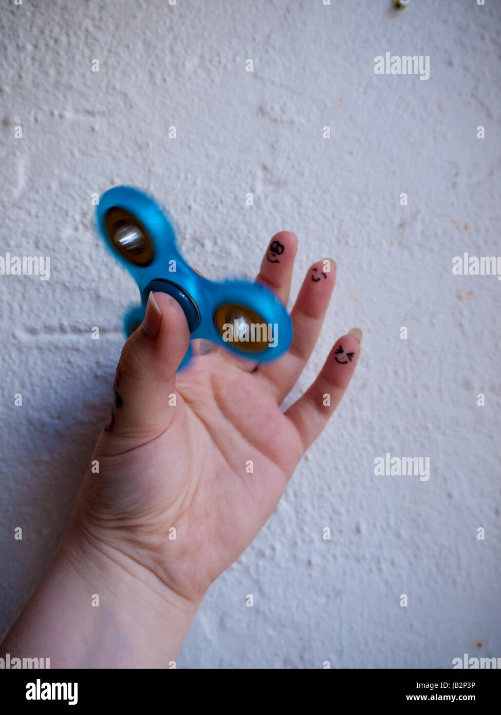 A moving fidget spinner in a hand with different smiling faces on the last three fingers Stock Photo