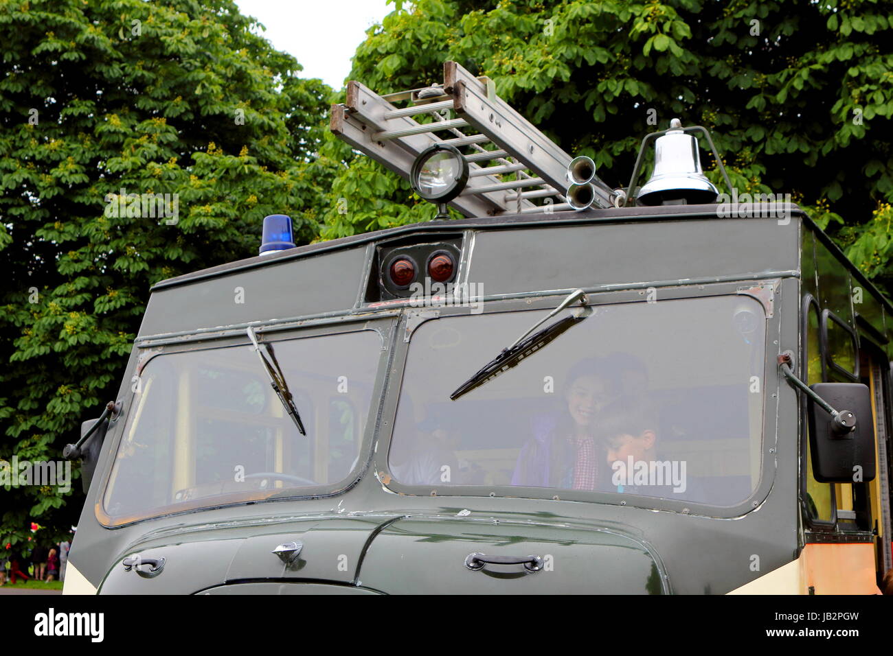 Beaulieu, Hampshire, UK - May 29 2017: Children in the cab of an antique British Fire Engine in military livery, also showing blue light, searchlight, Stock Photo