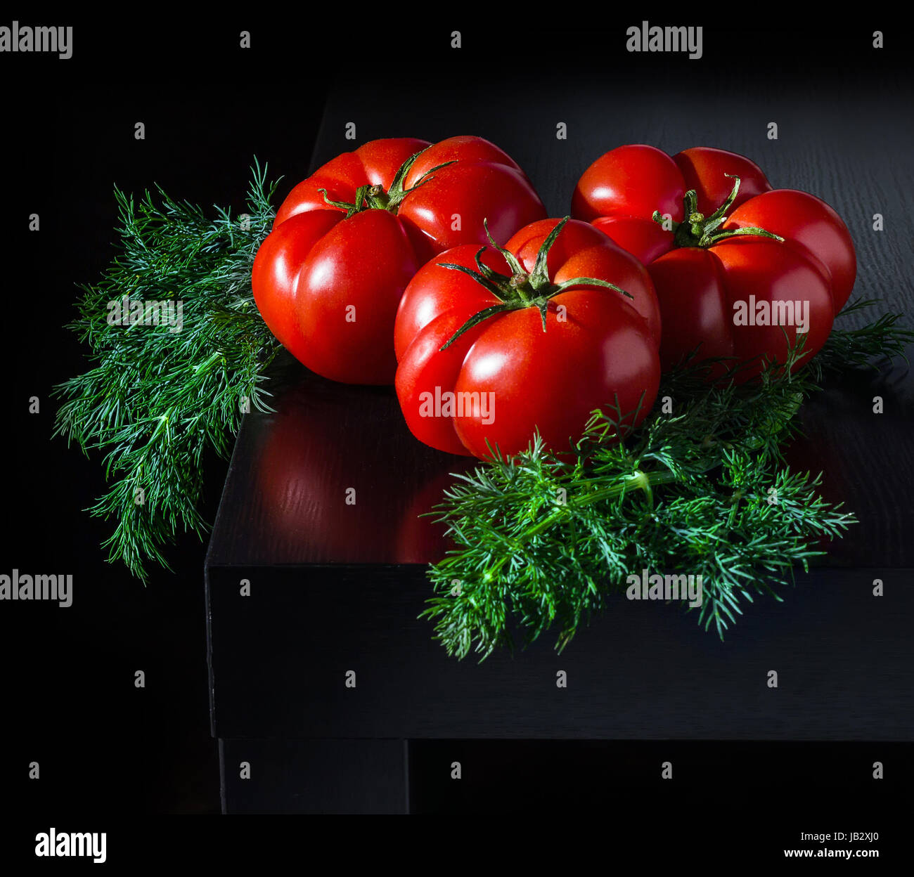 Three large fresh tomatoes and a sprig of dill on a dark wooden background Stock Photo