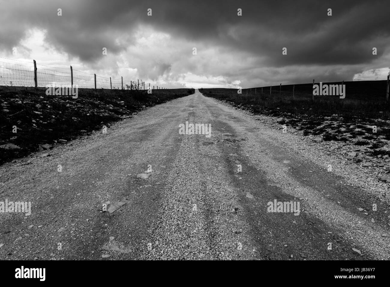 A long, country road, with no visible end, under a cloudy sky, taken as long exposure Stock Photo