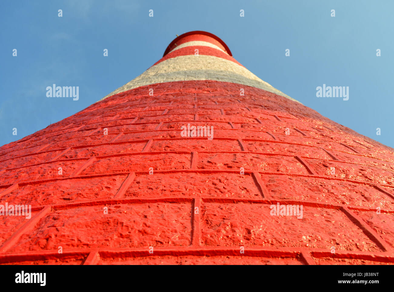A red and white light house towers into the light blue sky Stock Photo