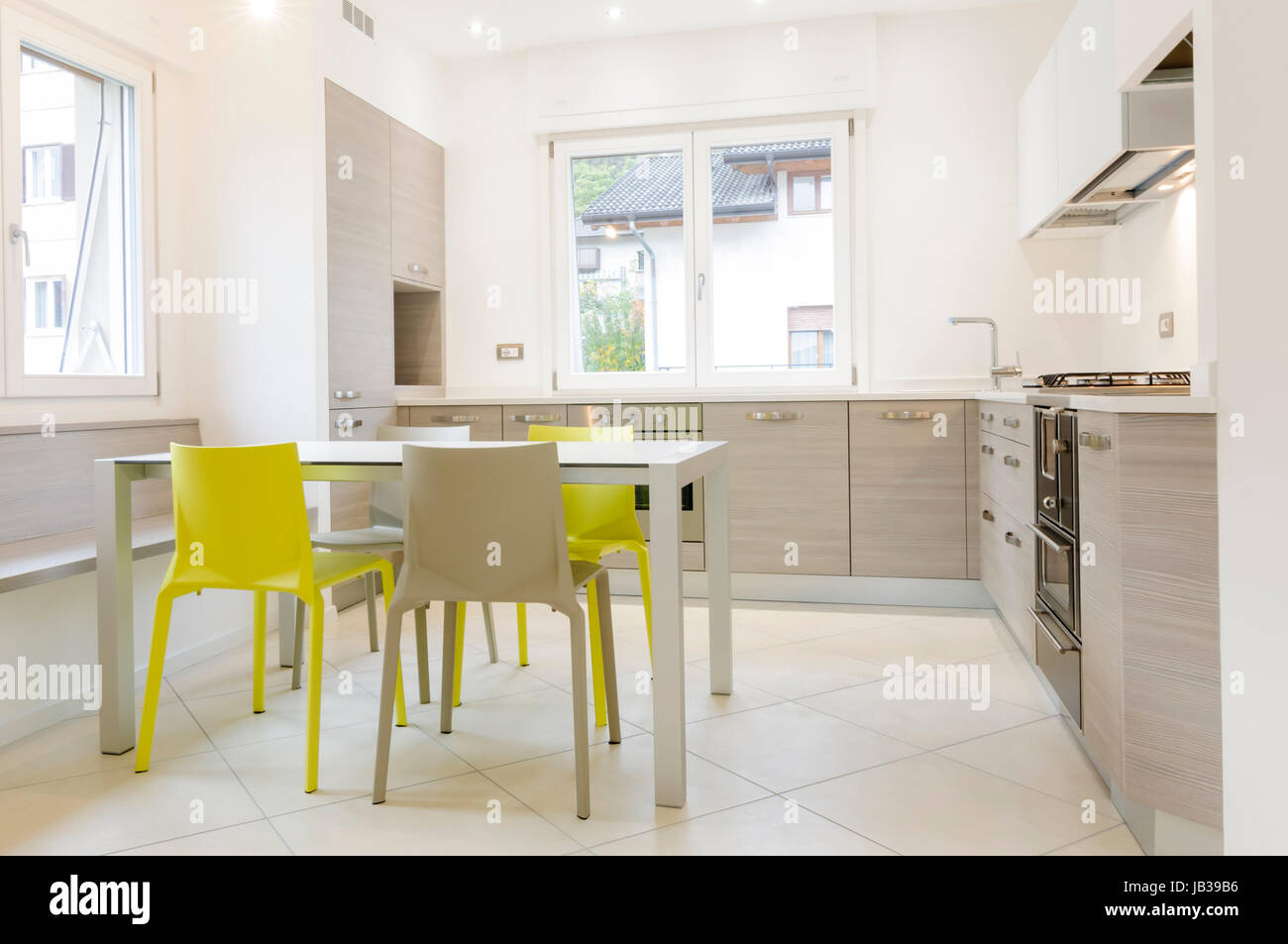 Modern kitchen interior with wooden cabinets, white table, grey and yellow chairs Stock Photo