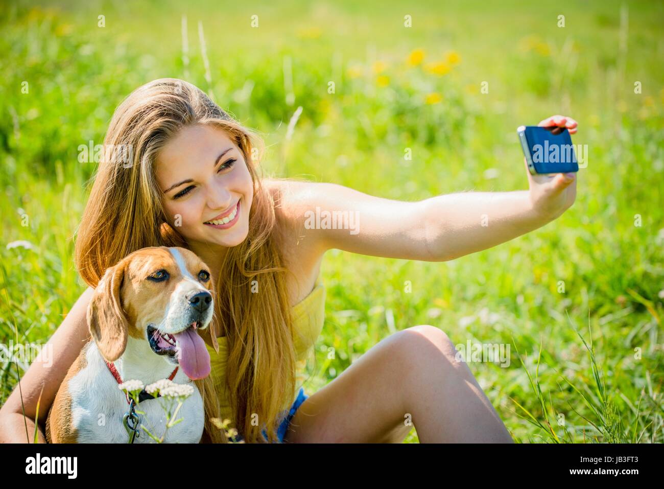 Teen girl taking photo of herself and her dog with mobile phone camera ...