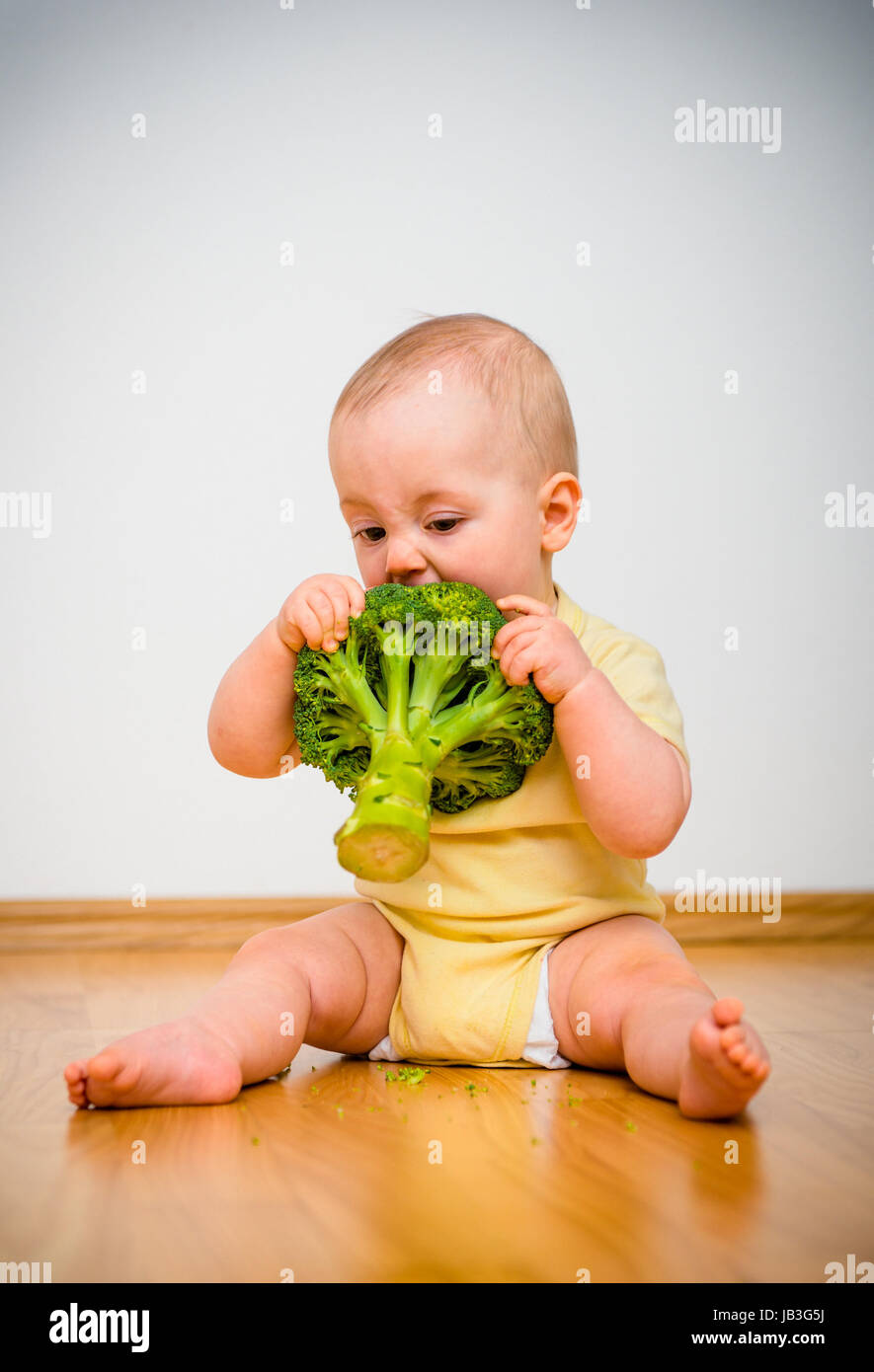 Cute baby eating broccoli sitting on floor indoors Stock Photo Alamy