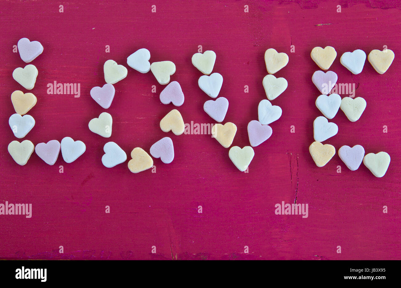 LOVE geschrieben mit herzfoermigen Bonbons auf rotem Hintergrund Stock Photo