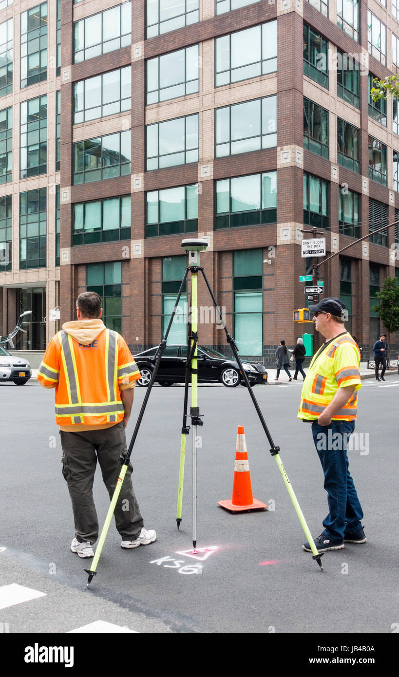 Two men in orange and yellow safety vests working with GPS on a tripod in Lower Manhattan Stock Photo