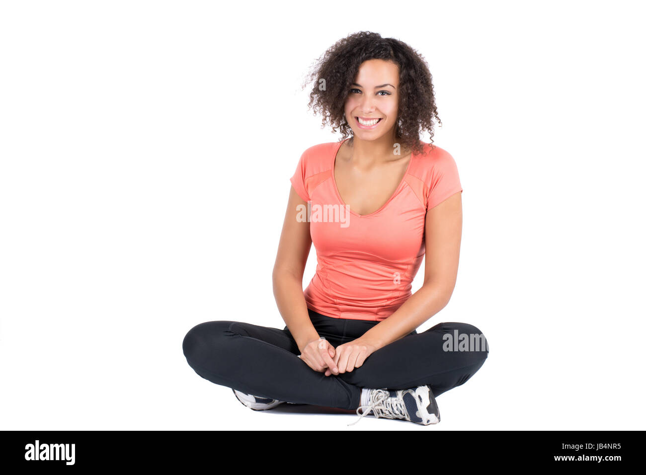 Freigestelltes Foto einer jungen Frau in Sportkleidung, die im Schneidersitz Platz genommen hat Stock Photo