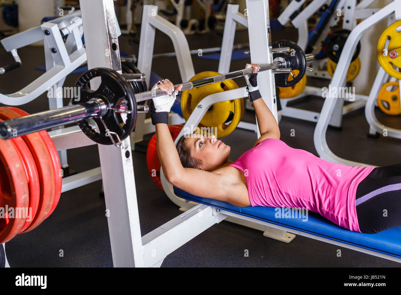 Sports young woman doing exercises with barbell on bench in the gym ...
