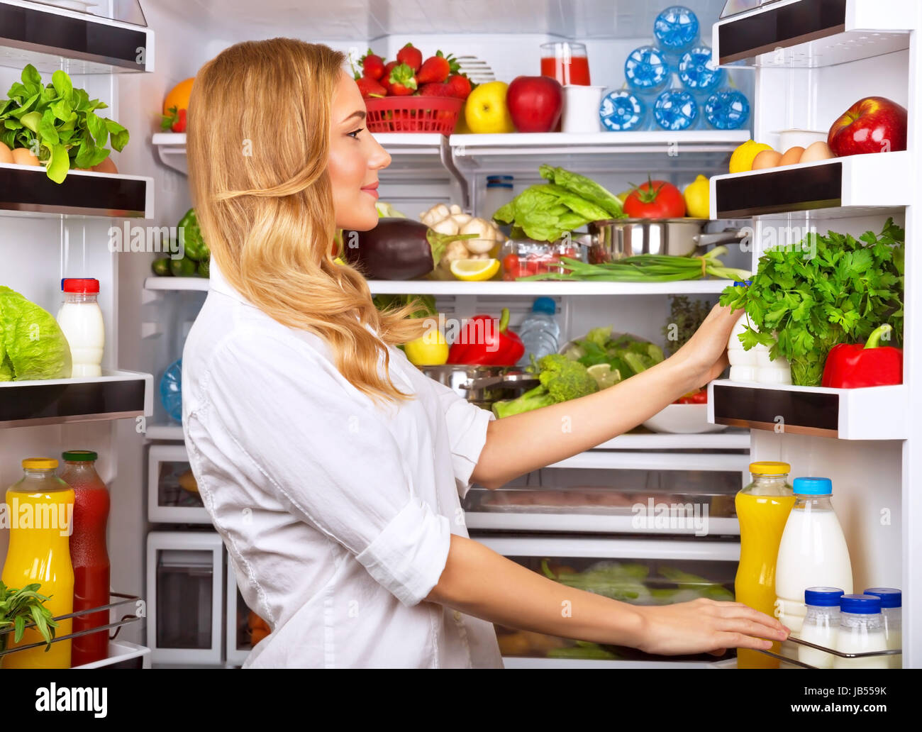 Happy female search something in the fridge, fresh fruits and vegetables in the refrigerator, cooking diet food, fit and body care concept Stock Photo