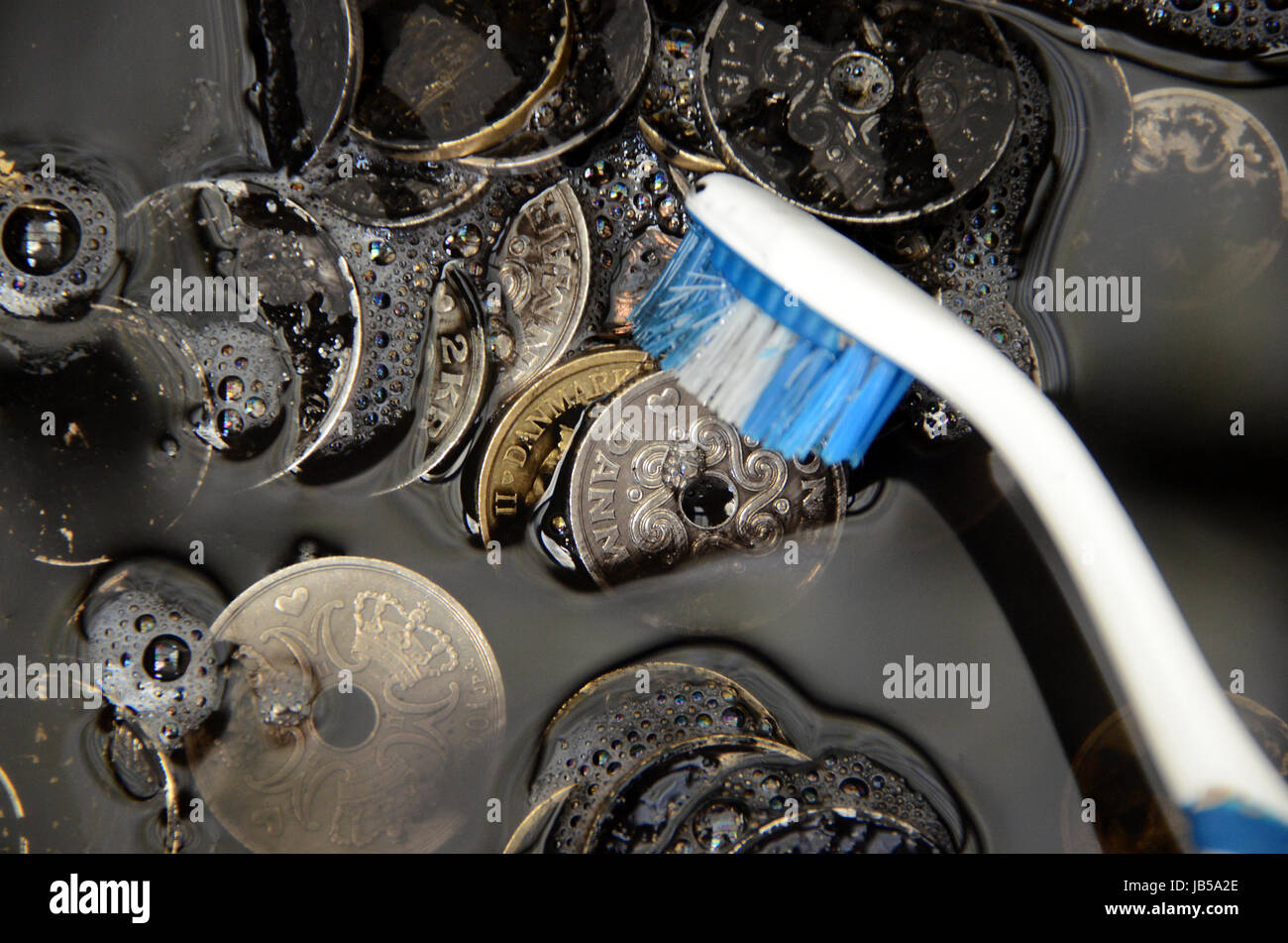 Black Danisk Krone coins being washed, suggesting the term 'whitewash of black money' Stock Photo