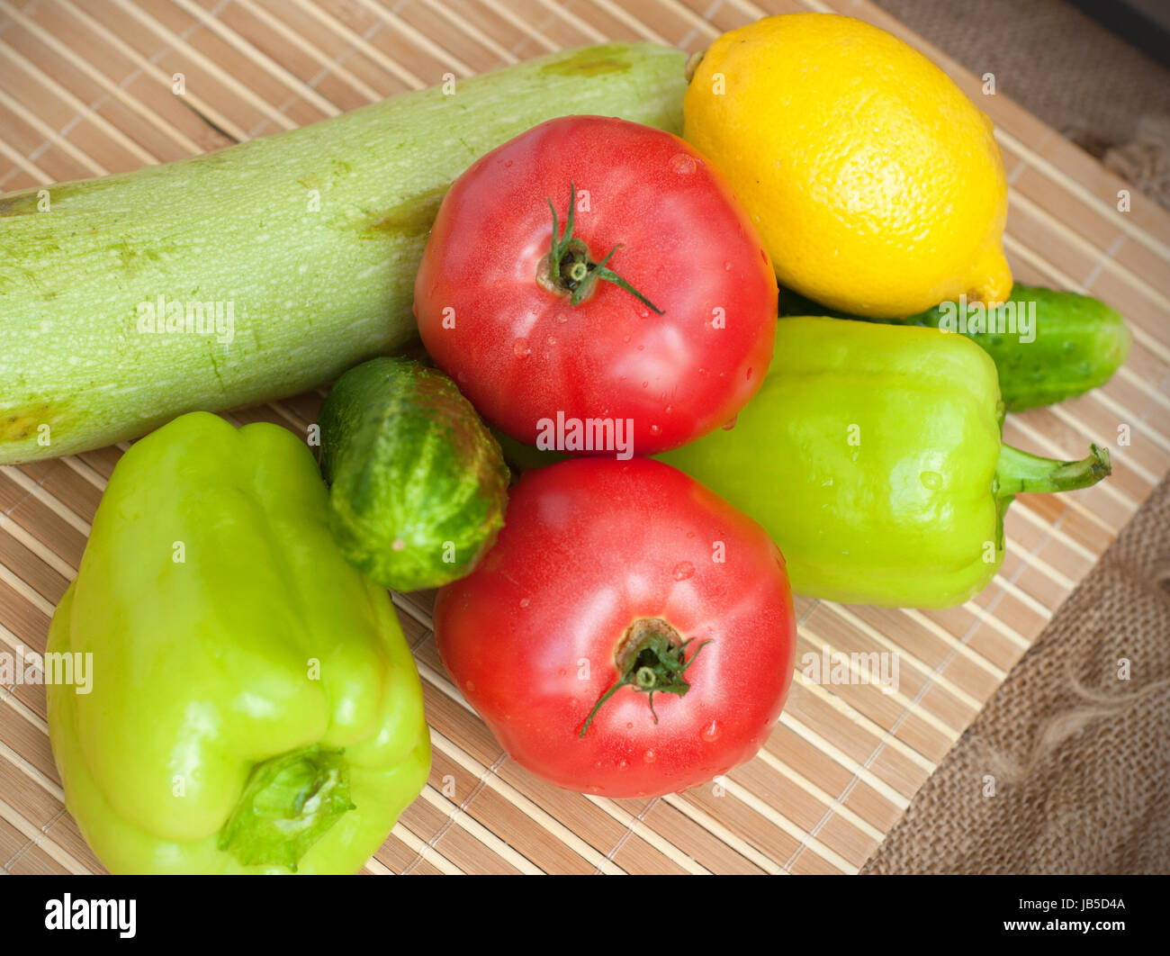 A group of tomatoes, cucumbers, green pepper, zucchini and a lemon on