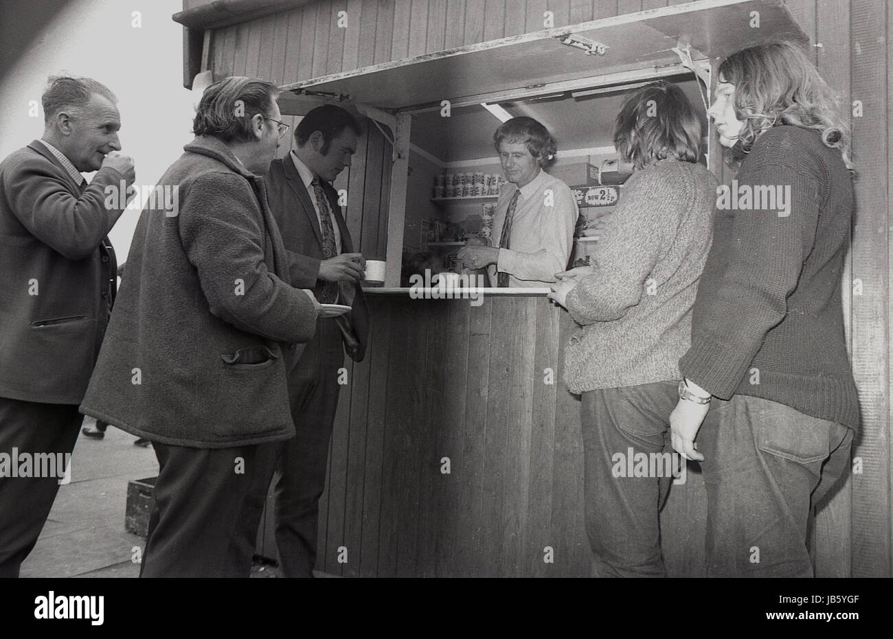 1973, historical picture, customers standing at the counter outside the famous Blackheath Tea Hut. A simple, basic snack bar, the small wooden hut with a service hatch for light food and beverages was a well known rest stop for people travelling on the A2 road at Greenwich, South London, SE3. An opportunity for a break, a cup of tea and some social interaction during one's journey. Stock Photo