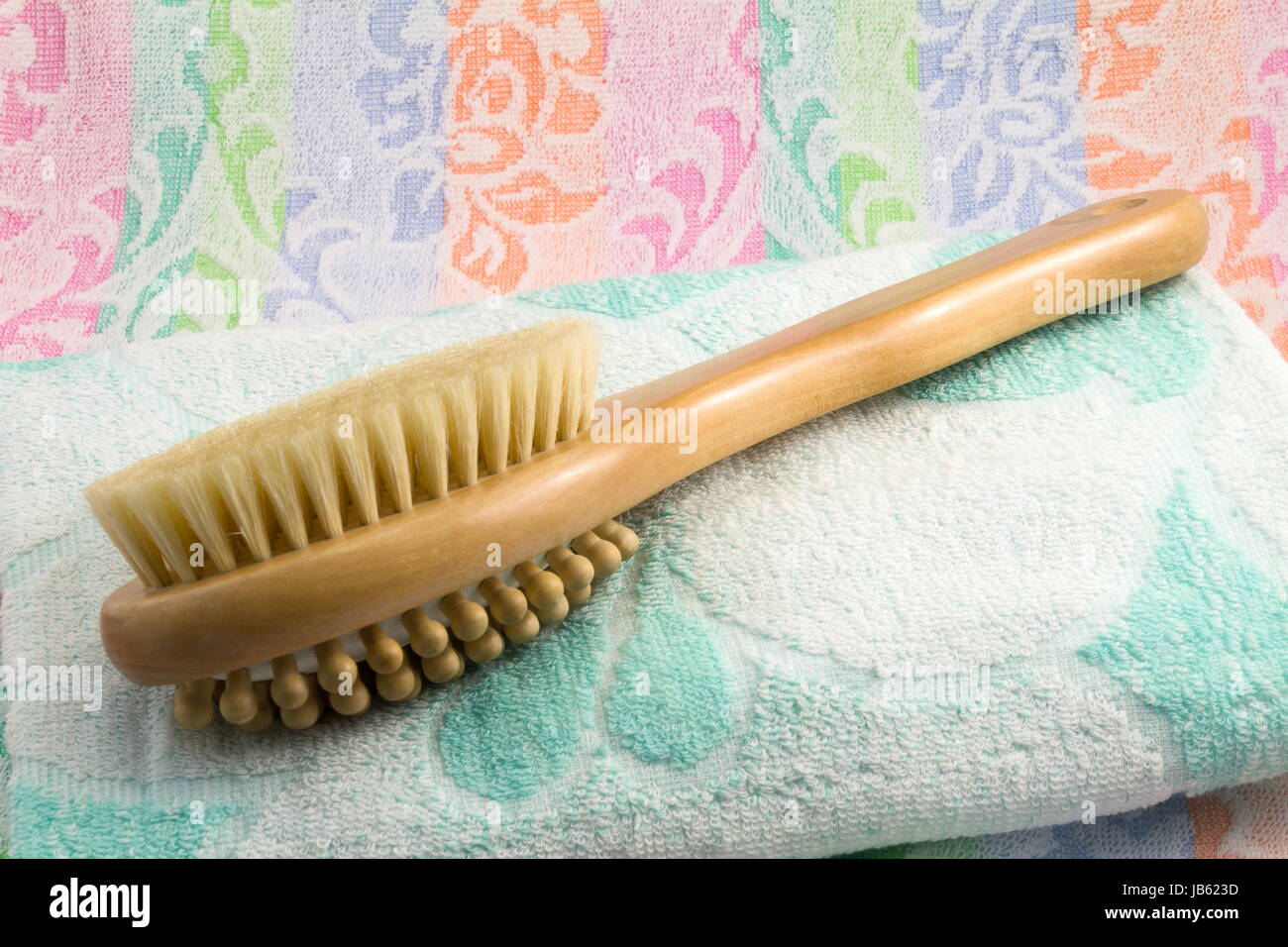 Wooden light brown brush with the long handle for body massage. Has wooden balls for massage and a rigid bristle for skin massage. Terry towel with an ornament. Stock Photo