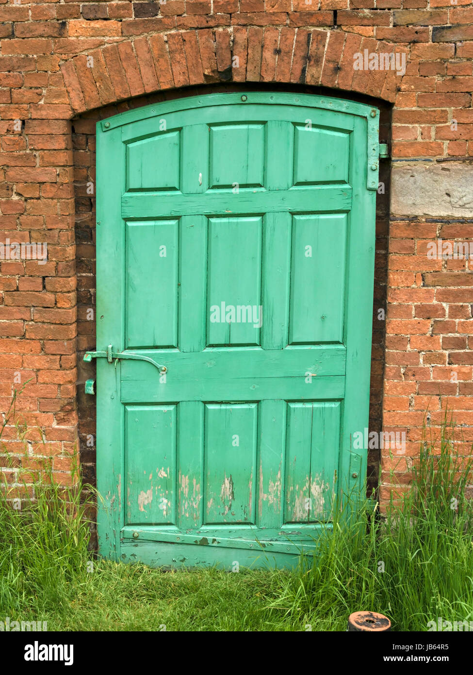 Old, green painted, panelled wooden door in red brick garden wall. Stock Photo