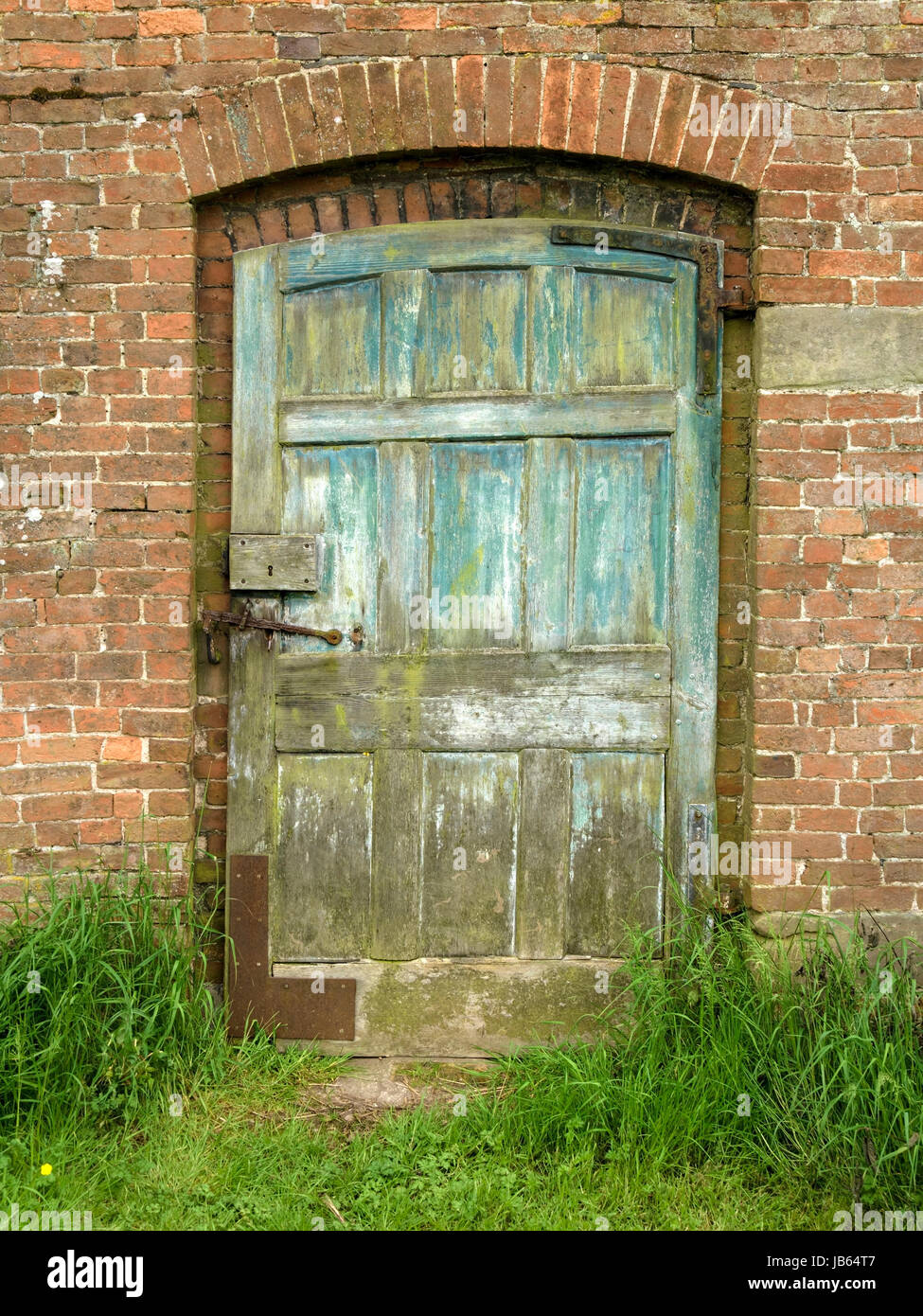 Old, distressed, peeling, painted, panelled wooden door in red brick garden wall. Stock Photo