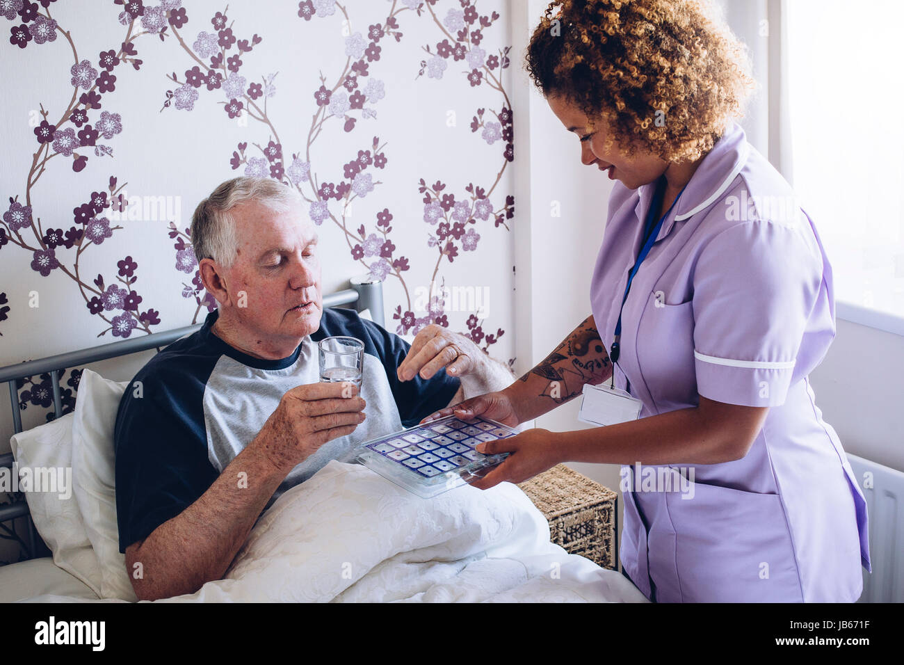 Bedbound senior man receiving assistance from a home caregiver. He is taking some medication with water. Stock Photo