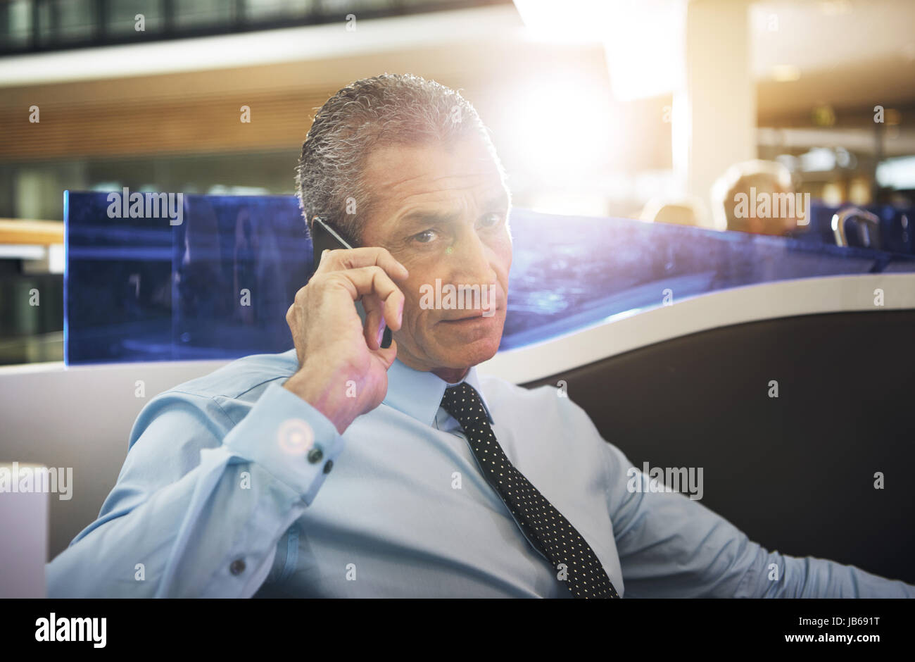 Mature businessman sitting in office and having phone conversation looking at camera. Stock Photo