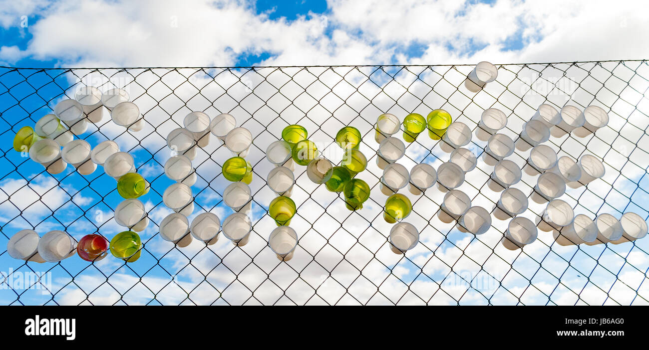 Green and white plastic cups on a fence spelling the spanish word for 'Smile' Stock Photo