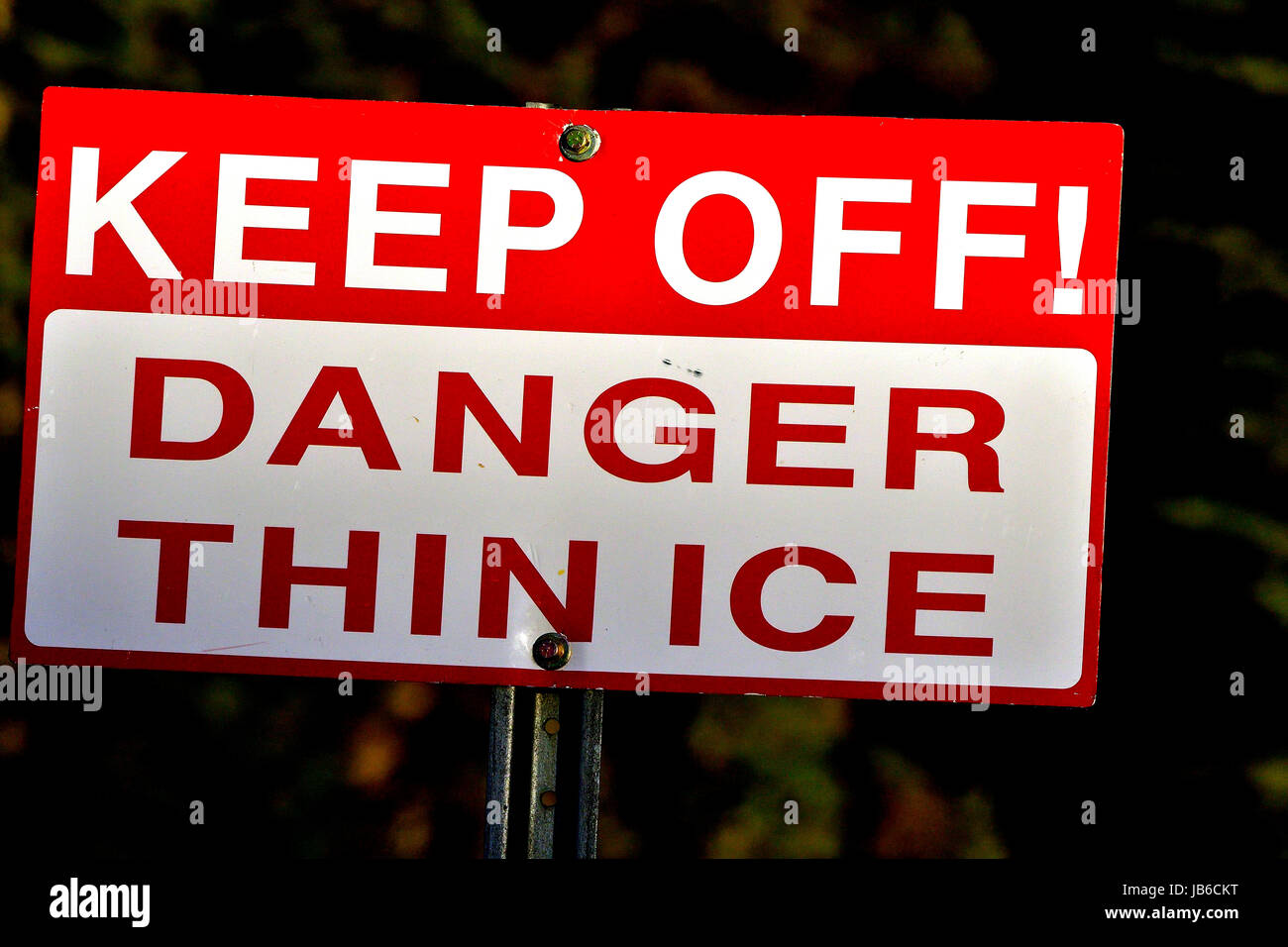 A red and white sign warning people that the ice is very thin and that they should keep off the lake Stock Photo
