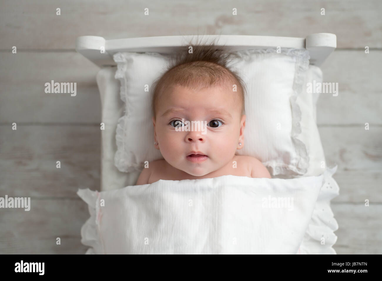 An overhead shot of a four month old, alert, baby girl. She is lying in a tiny bed and looking up at the camera. Stock Photo