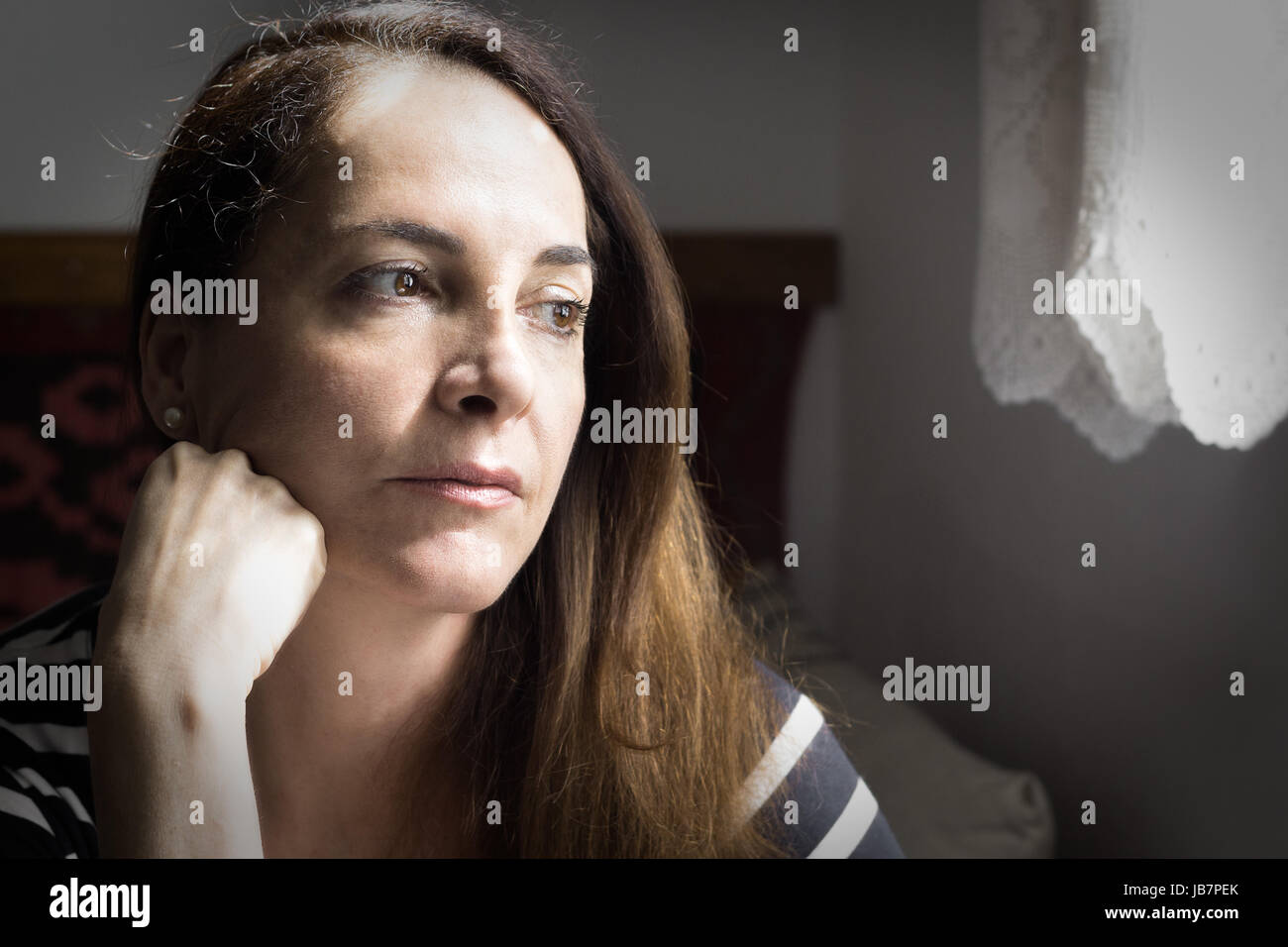 Portrait of a woman looking to a window and with a hand on her neck thinking with doubts, uncertain future Stock Photo